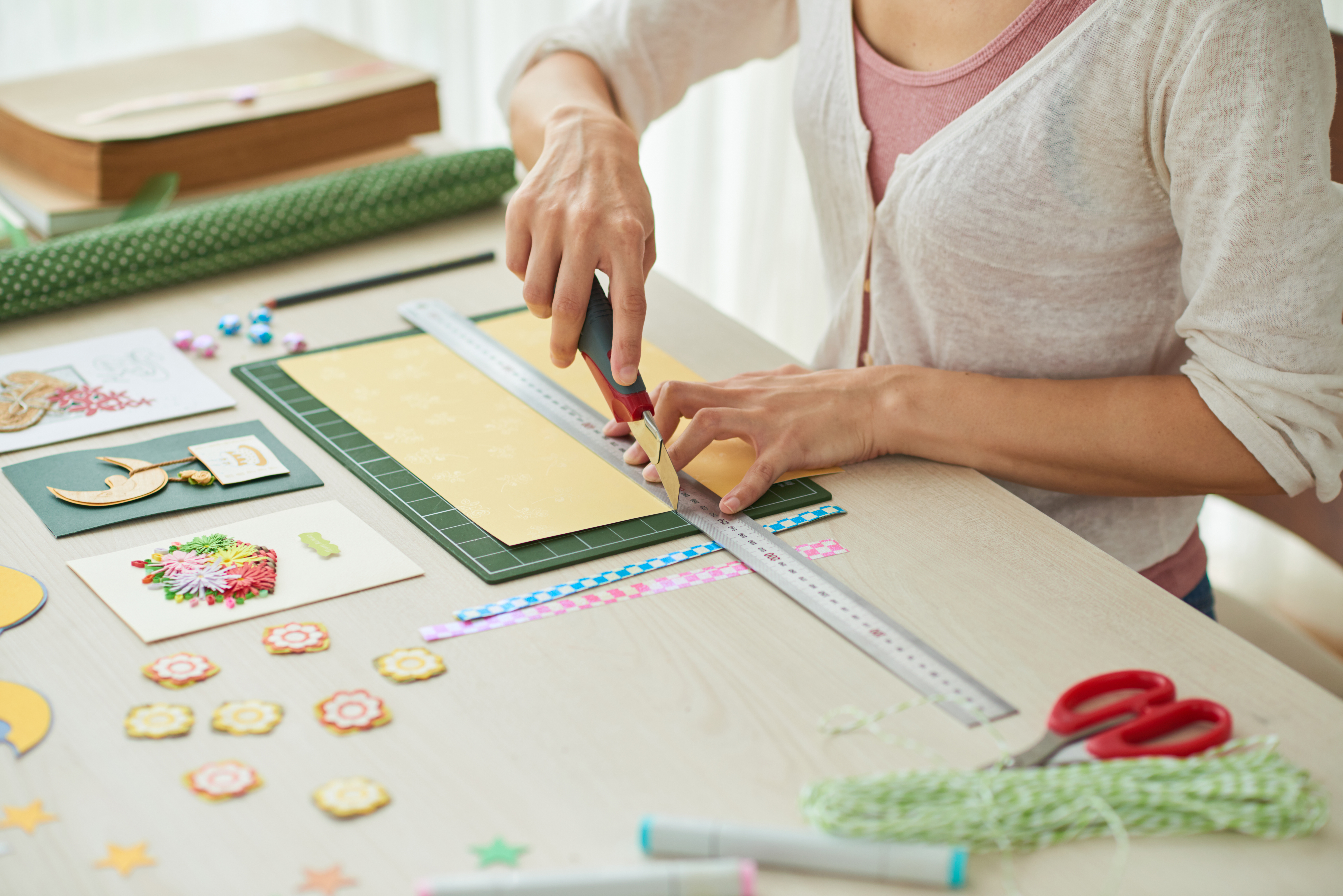 Creative woman sitting at wooden table and making greeting cards for her friends, scrapbooking items lying on surface